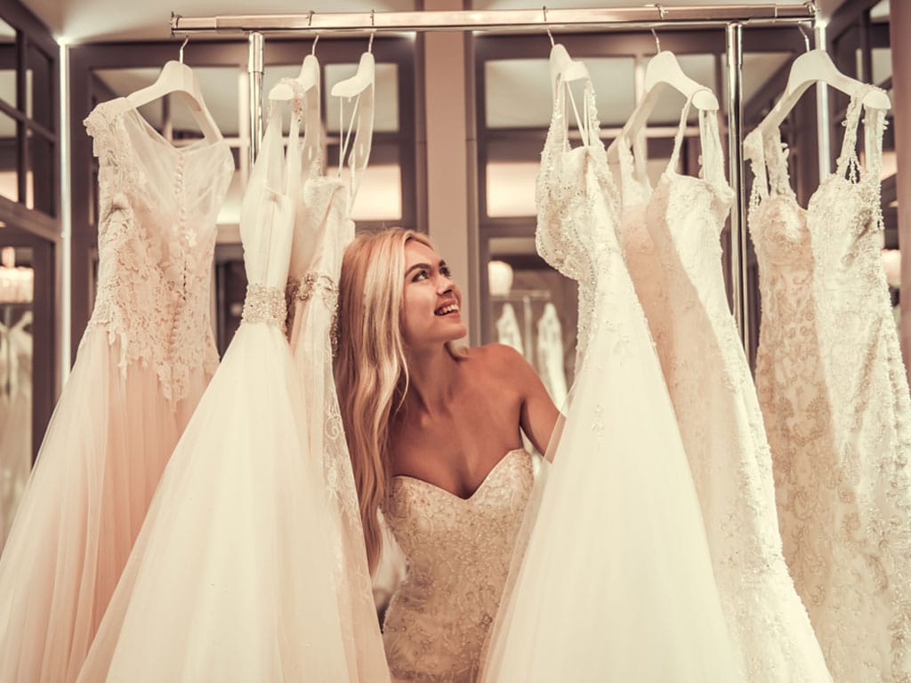 Brautkleid kaufen im Store – Braut beim Auswählen verschiedener Hochzeitskleider